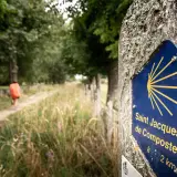 Panneau Saint Jacques de Compostelle sur le chemin, indiquant la direction de Conques. Un pèlerin s'éloigne sur le sentier.