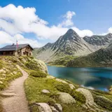 Sentier de randonnée en Andorre menant à un refuge de montagne près d'un lac alpin aux eaux bleues, avec des montagnes escarpées en arrière-plan.