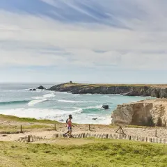 Deux randonneurs profitent du tour de la presqu'île de Quiberon à pied, longeant la côte rocheuse et la mer agitée sous un ciel bleu.