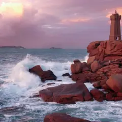 Phare de Ploumanac'h, un joyau pour visiter la Bretagne. Vagues s'écrasant sur les rochers roses sous un ciel pastel.