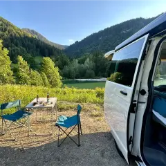 Un coin de paradis pour la Bourgogne en camping-car : table dressée, chaises bleues, lac paisible et montagnes verdoyantes.