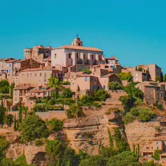 Village perché en Provence, idéal pour un budget vacances. Maisons en pierre, toits de tuiles, végétation luxuriante sous un ciel bleu.
