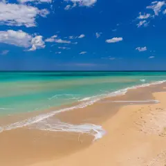 Plage de Bari, sable doré, eaux turquoise et ciel bleu azur avec des nuages blancs. Un rêve d'évasion.