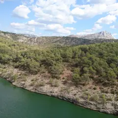 Vue panoramique du lac Zola, entouré de collines verdoyantes et rocheuses sous un ciel bleu parsemé de nuages blancs.