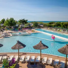Belle aire camping car à Marseillan avec piscines, transats et parasols. La mer est visible au loin.