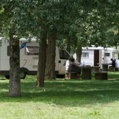 Des camping-cars stationnés dans un parc ombragé, des gens profitent de pique-niques. Un aperçu des plus belles aires de camping-car gratuites.