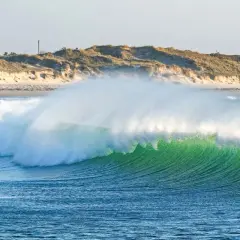 Vague verte et transparente, comme la pointe de la torche, déferlant sur une plage de sable et de dunes.