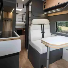 Intérieur d'un camping-car Bavaria : banquette confortable, table escamotable, plaque de cuisson et lit visible au fond.