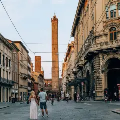 Un couple se promène dans une rue de Bologne, admirant les tours emblématiques. Une belle journée pour découvrir que faire à Bologne.