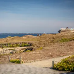 Vue panoramique sur la côte sauvage de la pointe Saint-Gildas, avec des falaises rocheuses, des dunes et la mer bleue. Des promeneurs profitent du paysage.