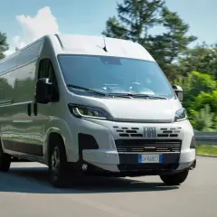 Un Fiat Ducato 2.2 Multijet 140 CV AdBlue blanc roule sur une route bordée d'arbres verts.