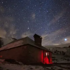 Un refuge illuminé par une lumière rouge sous un ciel étoilé. L'endroit parfait pour dormir en refuge après une longue journée.