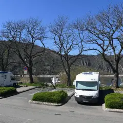 Stationnement pour camping-cars gratuit en Auvergne, avec vue sur le lac et les montagnes. Deux camping-cars sont garés sous des arbres dénudés.