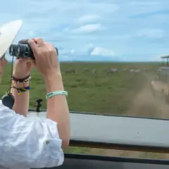 Une femme en safari, jumelles à la main, observe des zèbres en Tanzanie. Une excellente idée de que faire en Tanzanie !
