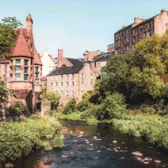 Un charmant ruisseau serpente à travers des bâtiments historiques en grès et une maison jaune vif. Idéal pour savoir que faire à Édimbourg.