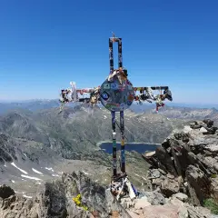 Croix ornée de souvenirs, au sommet d'une montagne, témoin d'un carlit randonnée mémorable. Paysage de haute altitude sous un ciel bleu.