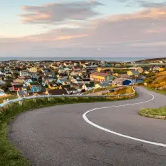 Vue panoramique de Saint-Pierre-et-Miquelon, avec ses maisons colorées nichées sur la côte et une route sinueuse menant au village.
