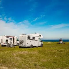 Plusieurs camping-cars stationnés sur une aire de camping car gratuite, face à la mer sous un ciel bleu.