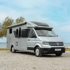 Camping car petite taille Adria Compact Max argenté, garé sur un chemin de gravier près de la mer.
