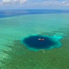 Un bateau rouge et blanc flotte au-dessus du trou du dragon, un abîme bleu profond entouré de récifs coralliens turquoise.