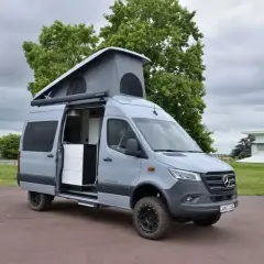 Camping car 4x4 gris avec toit relevable ouvert, prêt pour l'aventure.