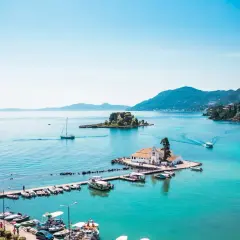 Vue idyllique de la baie de Corfou avec des bateaux, une église sur un îlot et des collines verdoyantes. Idéal pour savoir que faire à Corfou.