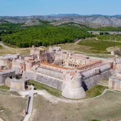 Vue aérienne du Fort de Salses, une imposante citadelle sur la côte vermeille, entourée de verdure et de collines.