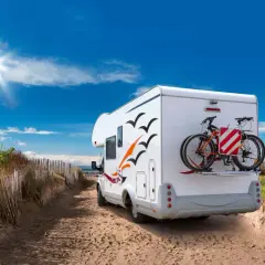 Camping-car prêt pour l'aventure sur une aire de camping car Ile de Ré, avec vélos à l'arrière, sous un ciel bleu éclatant.