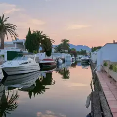 Coucher de soleil paisible sur les canaux d'Empuriabrava, Espagne, avec des bateaux amarrés et des palmiers se reflétant dans l'eau calme.