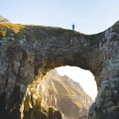 Un homme seul au sommet de la pointe de Dinan, surplombant un arc rocheux naturel.
