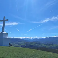 Le tuc de Montcalivert domine un paysage verdoyant sous un ciel bleu zébré de traînées de condensation. Une grande croix blanche se dresse fièrement.
