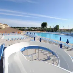 Piscine et toboggans aquatiques dans une aire de camping-car au Grau-du-Roi. Des chaises longues bleues et des parasols sont disposés autour des bassins.