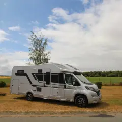 Camping-car Adria Matrix 670 SC argenté, stationné dans un champ sous un ciel nuageux.