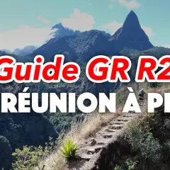 Guide GR R2 : La Réunion à pied, un randonneur sur un sentier escarpé avec des montagnes majestueuses en arrière-plan.