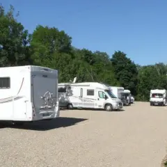 Stationnement de camping-cars sous un ciel bleu, avec des arbres en arrière-plan. Une aire camping car Arras paisible pour les voyageurs.