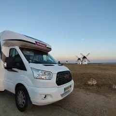Un camping-car blanc est garé devant des moulins à vent au coucher du soleil. Un voyage en camping-car inoubliable.