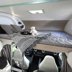 Lit pavillon confortable dans un camping-car, prêt pour une nuit paisible. Un ours en peluche veille sur le sommeil.