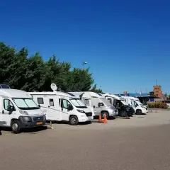 Rangée de camping-cars blancs et gris garés sous un ciel bleu clair.