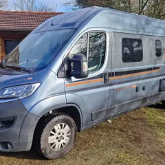 Un camping-car gris, modèle Globecar, est garé devant une maison en bois. Il est prêt pour une aventure avec son look d'Argus.