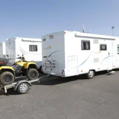 Un quad jaune sur une remorque, prêt à être tracté par un camping-car. Le quad est bien attaché, prêt pour l'aventure, comme indiqué sur la carte grise.