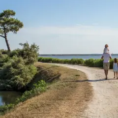 Une famille profite d'une randonnée à Arcachon, longeant un cours d'eau sous un ciel bleu.