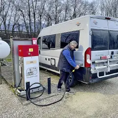 Un homme fait le plein de son camping-car à une installation GPL. Le véhicule est garé à côté d'une pompe à carburant rouge et blanche.