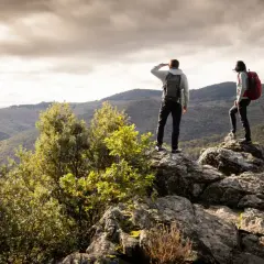 Deux randonneurs contemplent un paysage montagneux depuis un promontoire rocheux, profitant d'une vue panoramique.