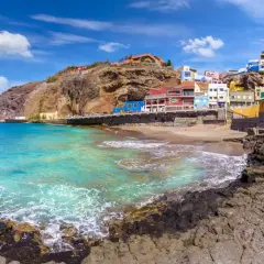 Plage de sable, maisons colorées accrochées à flanc de falaise, eaux turquoise. Idéal pour savoir que faire aux Canaries.