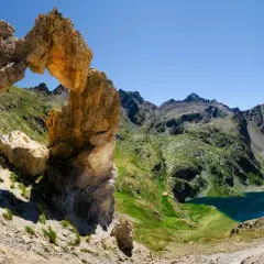 Un arc rocheux spectaculaire domine un paysage de montagne verdoyant, avec des lacs bleus scintillants. Une vue digne d'une carte du Mercantour.