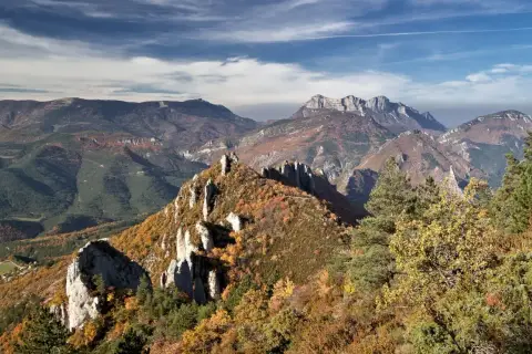 Vue panoramique des gorges de la Roanne en automne. Un sentier de randonnée serpente à travers des crêtes rocheuses et des forêts aux couleurs flamboyantes.