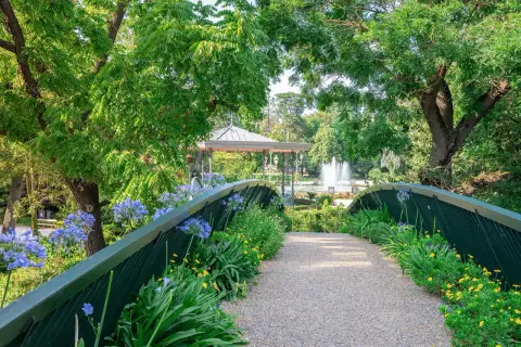 Un pont fleuri mène à un kiosque et une fontaine au jardin des plantes de Toulouse.