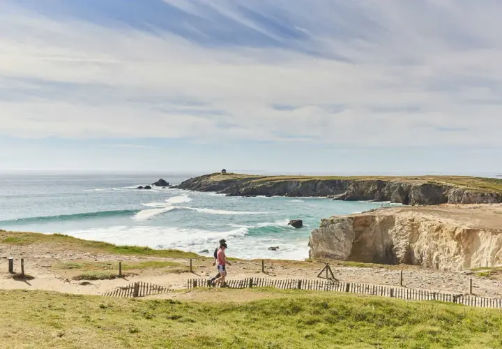 Deux randonneurs profitent du tour de la presqu'île de Quiberon à pied, longeant la côte rocheuse et la mer agitée sous un ciel bleu.