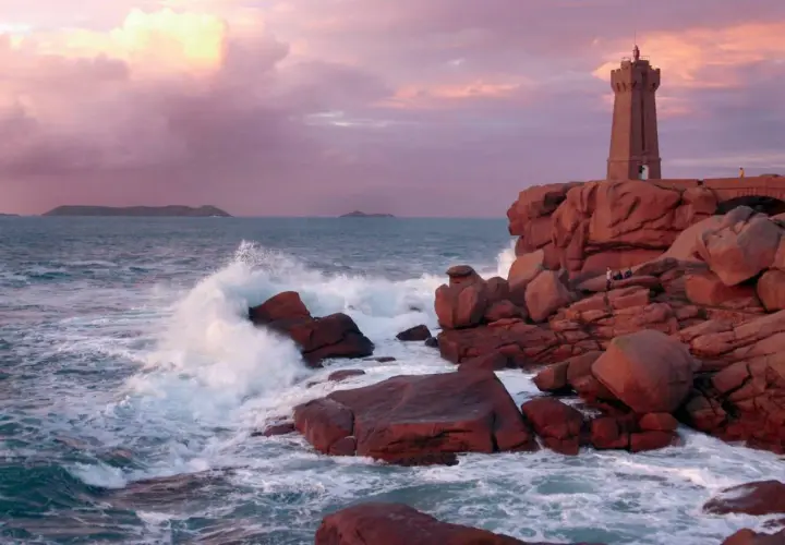 Phare de Ploumanac'h, un joyau pour visiter la Bretagne. Vagues s'écrasant sur les rochers roses sous un ciel pastel.