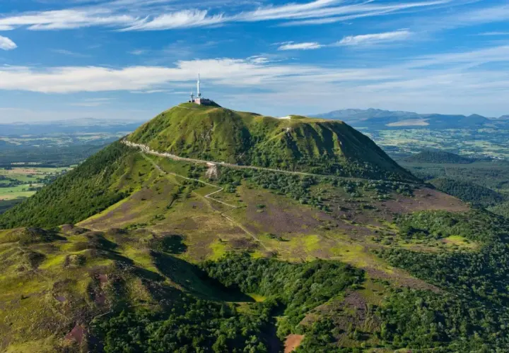 Vue aérienne du Puy de Dôme, un des volcans d'Auvergne, avec sa route en lacets et son antenne. Paysage verdoyant sous un ciel bleu.